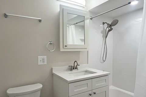 A white bathroom with a toilet, sink, mirror, and shower.