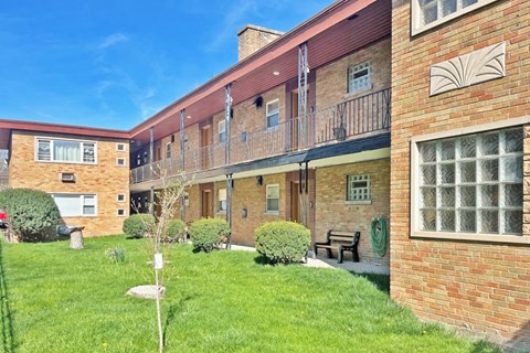 a brick apartment building with a green yard and a bench