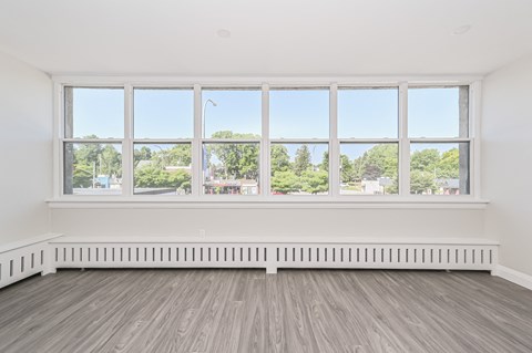 A room with a large window overlooking a street with trees and buildings.