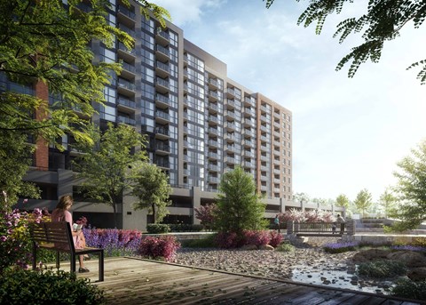 A woman sits on a bench in a park-like setting in front of a large building.