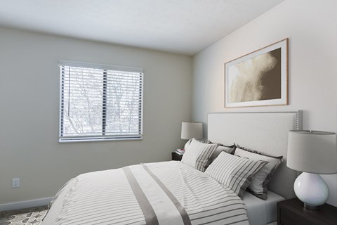 A bedroom with a bed, a painting on the wall, two lamps, and a window allowing natural light in Valparaiso, IN.