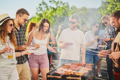 A group of people are gathered around a barbecue grill, enjoying a sunny day outdoors.