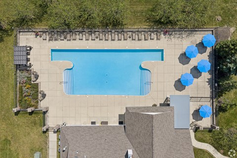 A large swimming pool surrounded by a concrete patio and blue umbrellas.