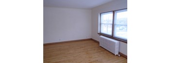 an empty room with a wood floor and a radiator and two windows