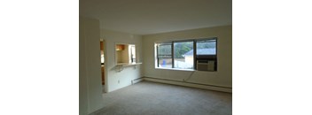 an empty living room with a large window and a kitchen