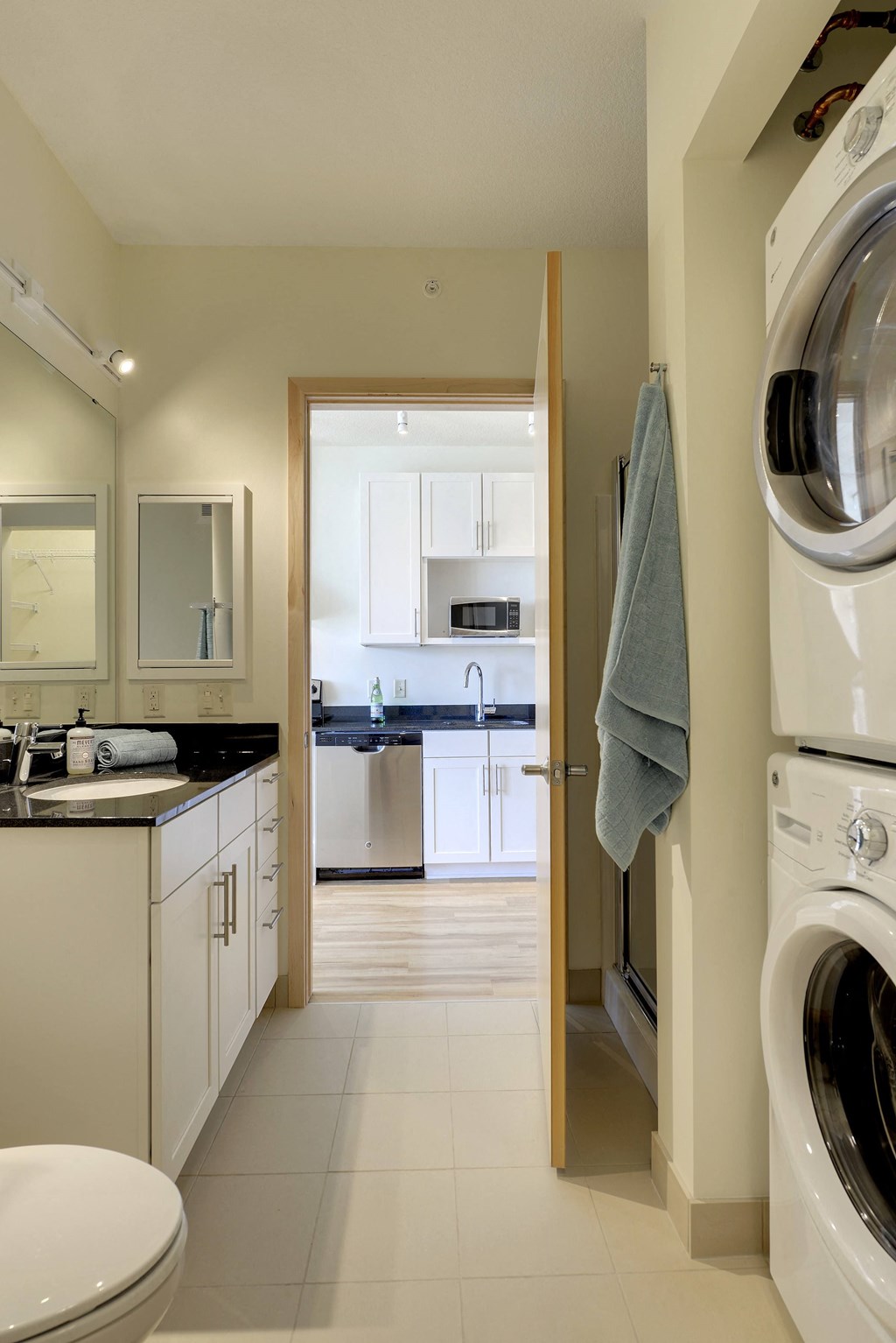 Bathroom with washer dryer stack, stand up shower, toilet in the Flat B studio floor plan at Coze Flats. View of kitchen across the hallway from the open bathroom door.