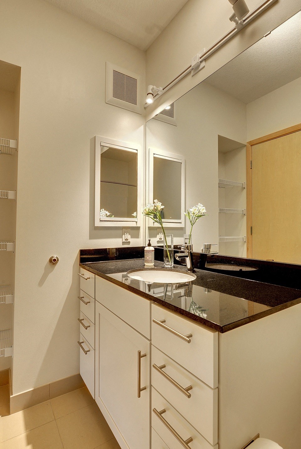 Bathroom in Flat J at Coze Flats with white cabinets, mirror and black granite countertops