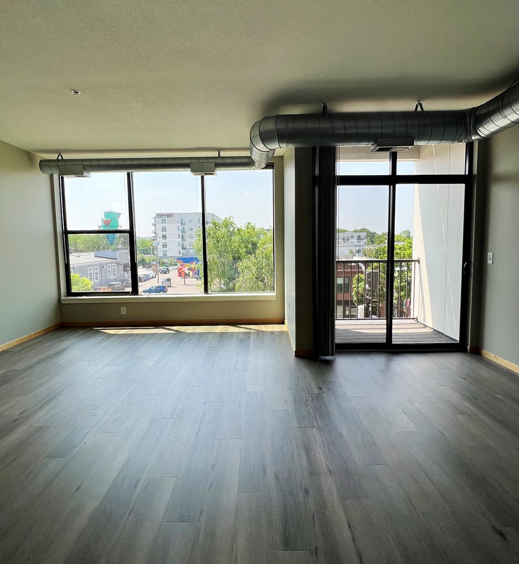 an empty living room with wood floors and large windows
