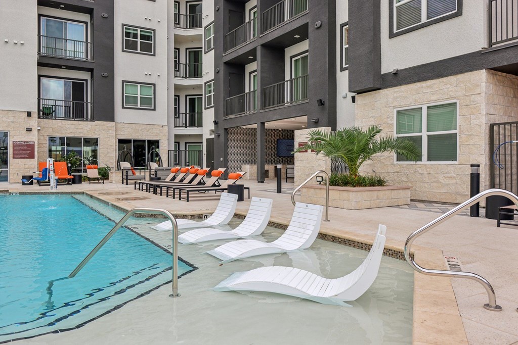 A pool with white chairs and a building in the background.