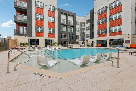 A pool with lounge chairs in front of a building.