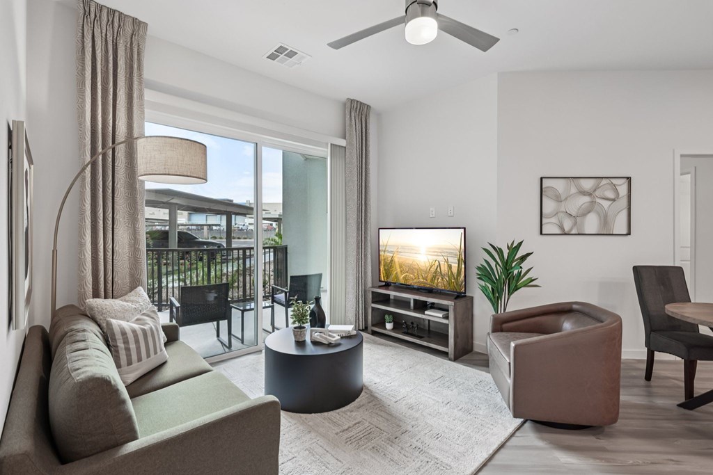 A living room with a grey sofa, a round coffee table, a television, and a ceiling fan.