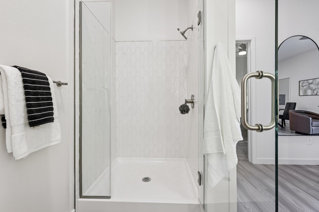 A white bathroom with a glass shower door and a white towel hanging on the wall.