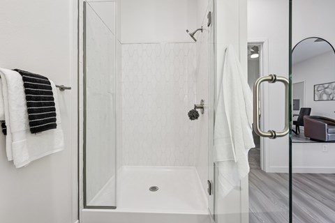 A white bathroom with a glass shower door and a white towel hanging on the wall.