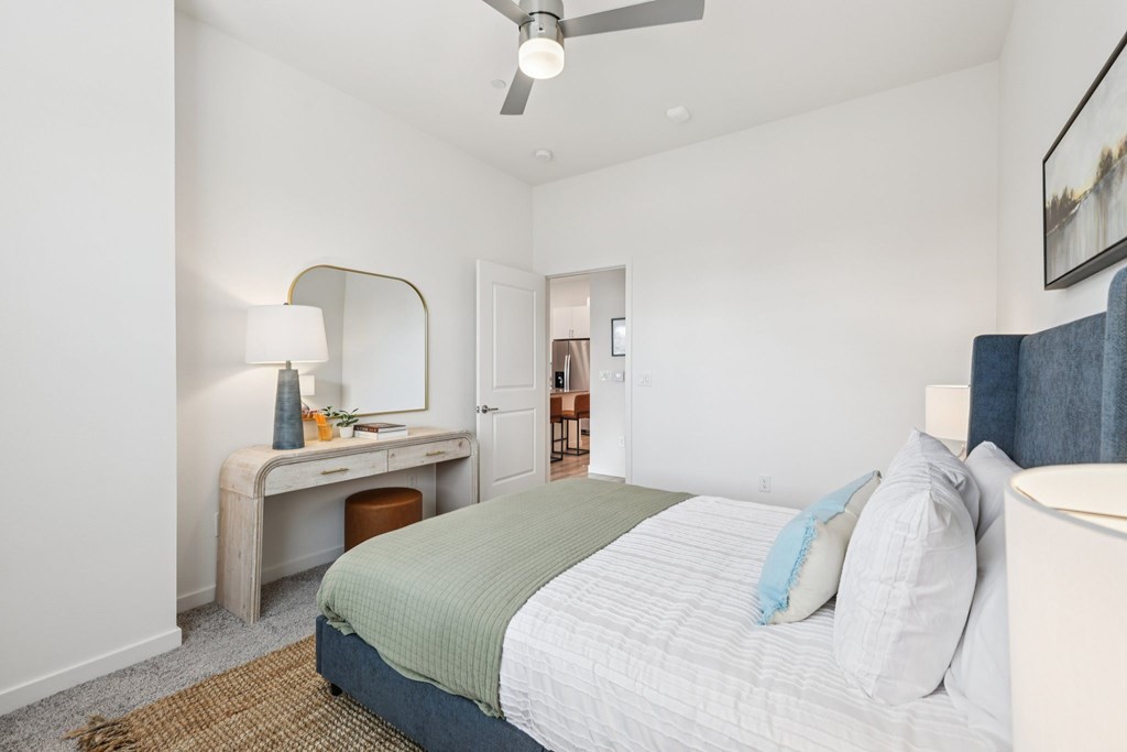 A bedroom with a bed, desk, and mirror.