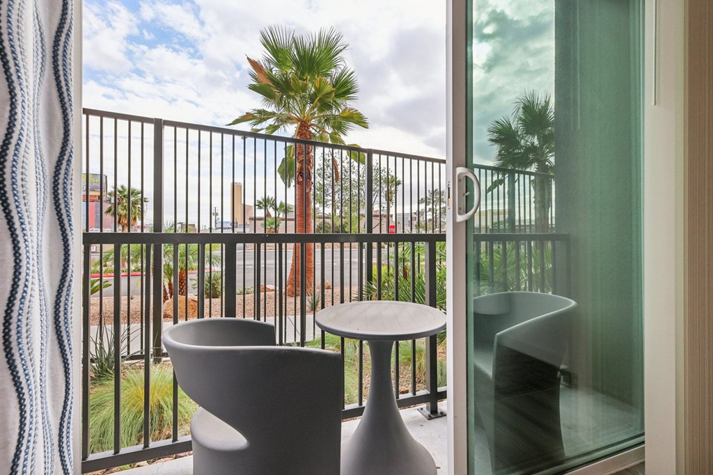 A balcony with a table and chairs overlooking a palm tree.