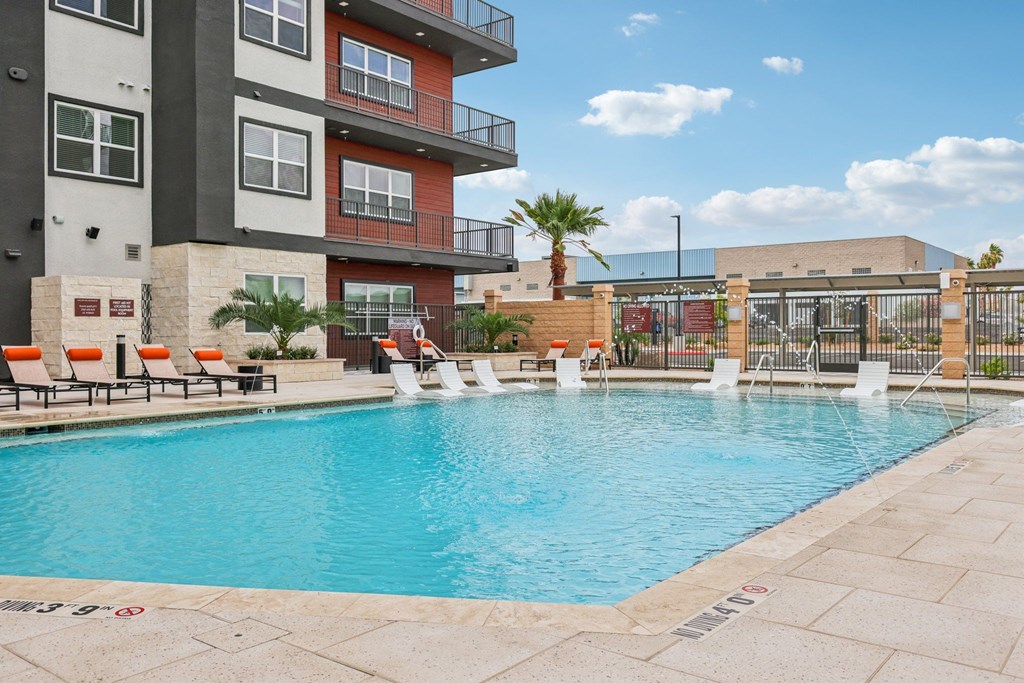 A pool surrounded by a patio and chairs in front of a building.