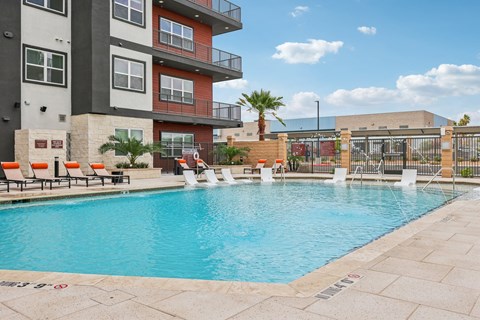 A pool surrounded by a patio and chairs in front of a building.