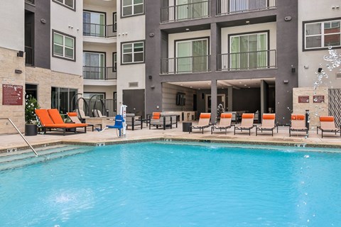 A swimming pool in front of a building with orange lounge chairs around it.