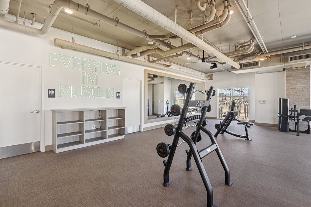 A gym with a neon sign that says "Everyday I'm muscini" on the wall.