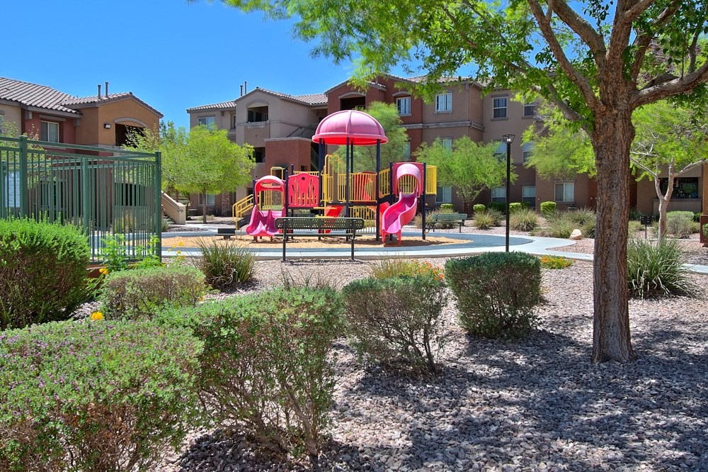 a playground with a red and yellow swing set in a park