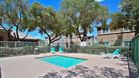 A pool surrounded by trees and chairs.