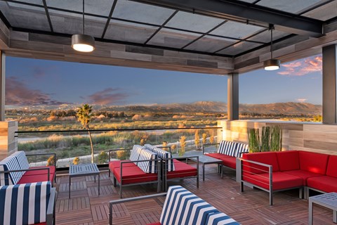 A patio with red couches and striped chairs overlooks a scenic view.