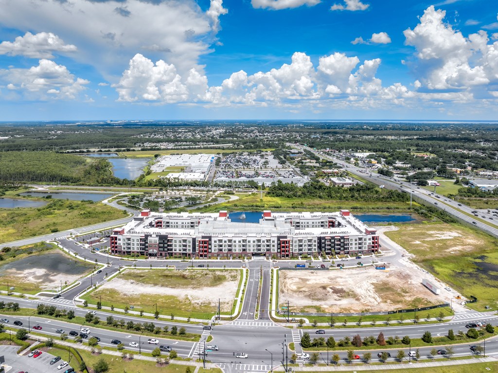 A large building with a red roof is surrounded by a parking lot and a body of water.