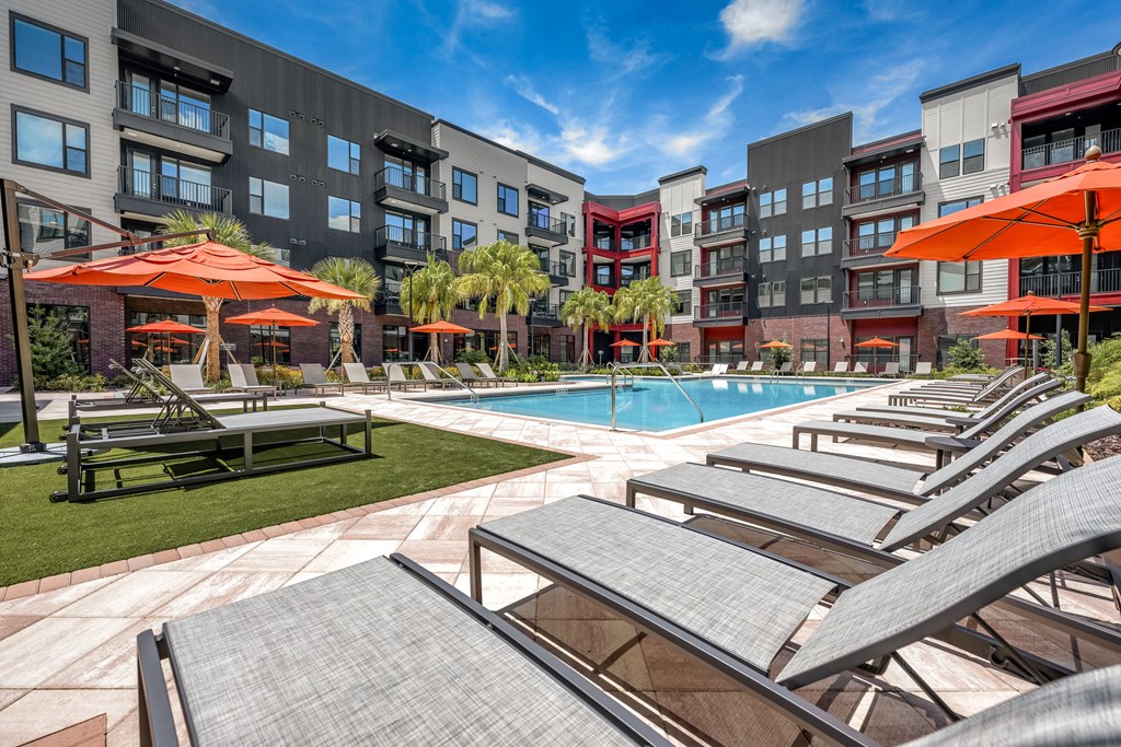 A pool surrounded by sun loungers and umbrellas in front of apartment buildings.