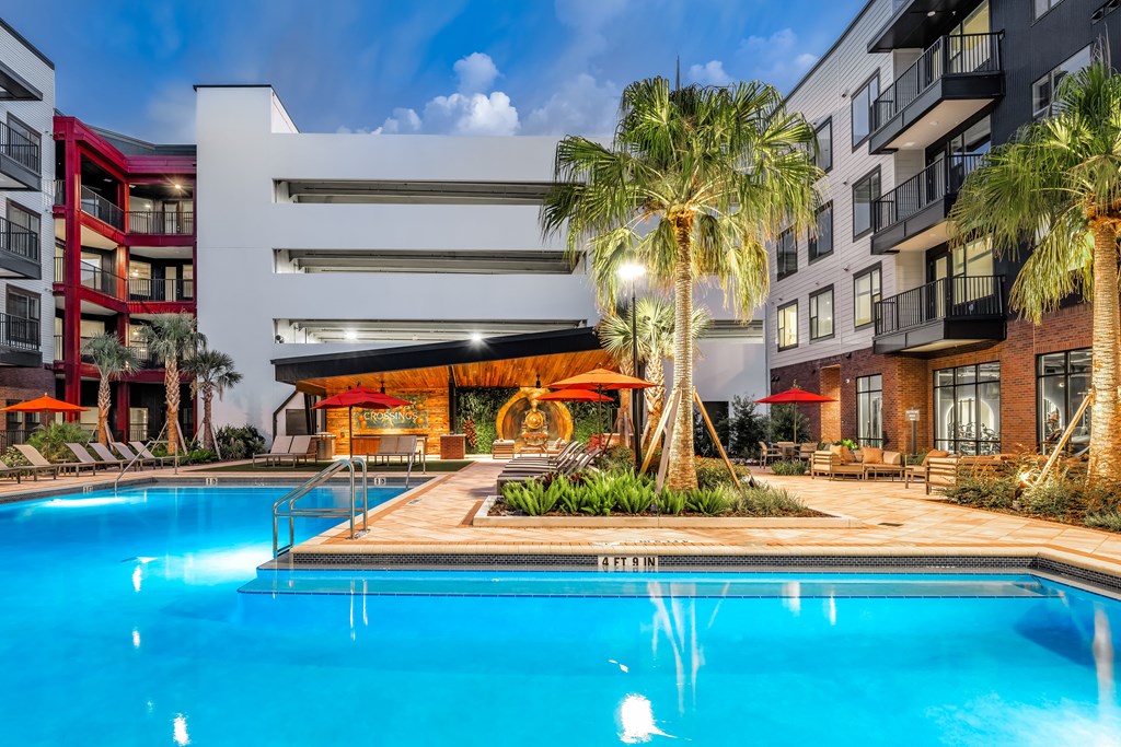 A swimming pool in front of a modern building with palm trees.