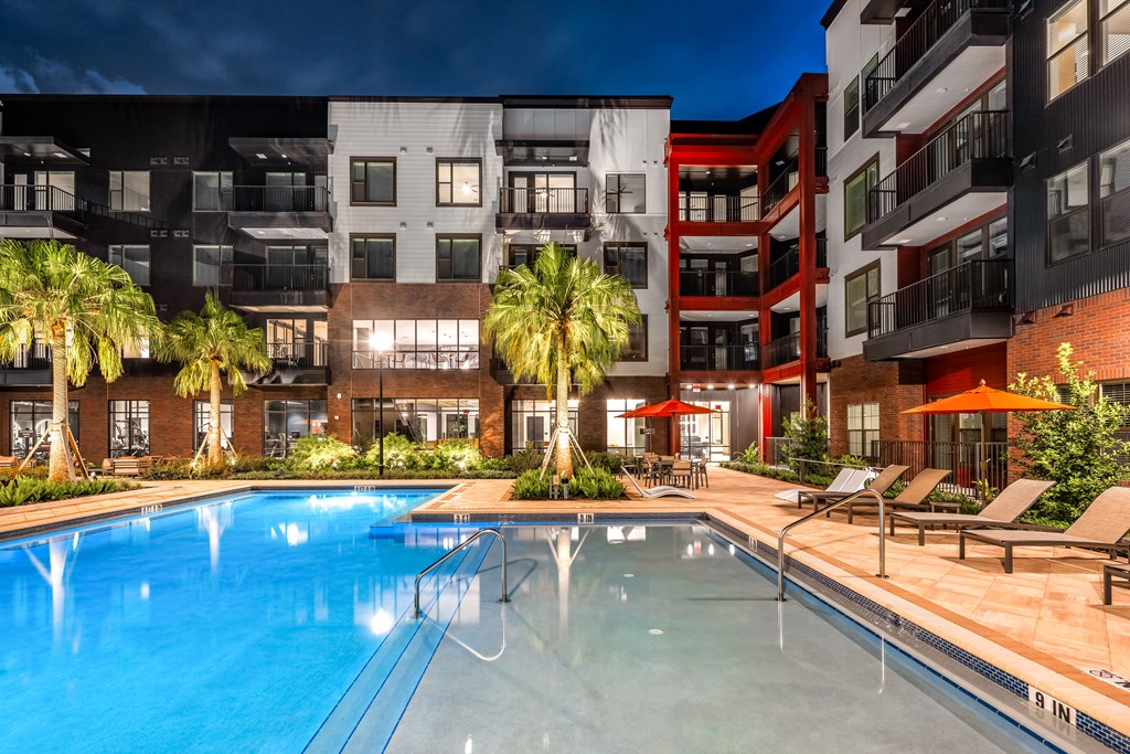 A swimming pool in front of a building with a red umbrella.