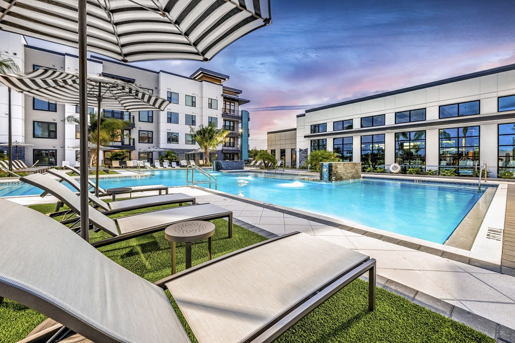 a swimming pool with lounge chairs and umbrellas in front of an apartment building at The Alibi at Lake Lilly, Ocoee