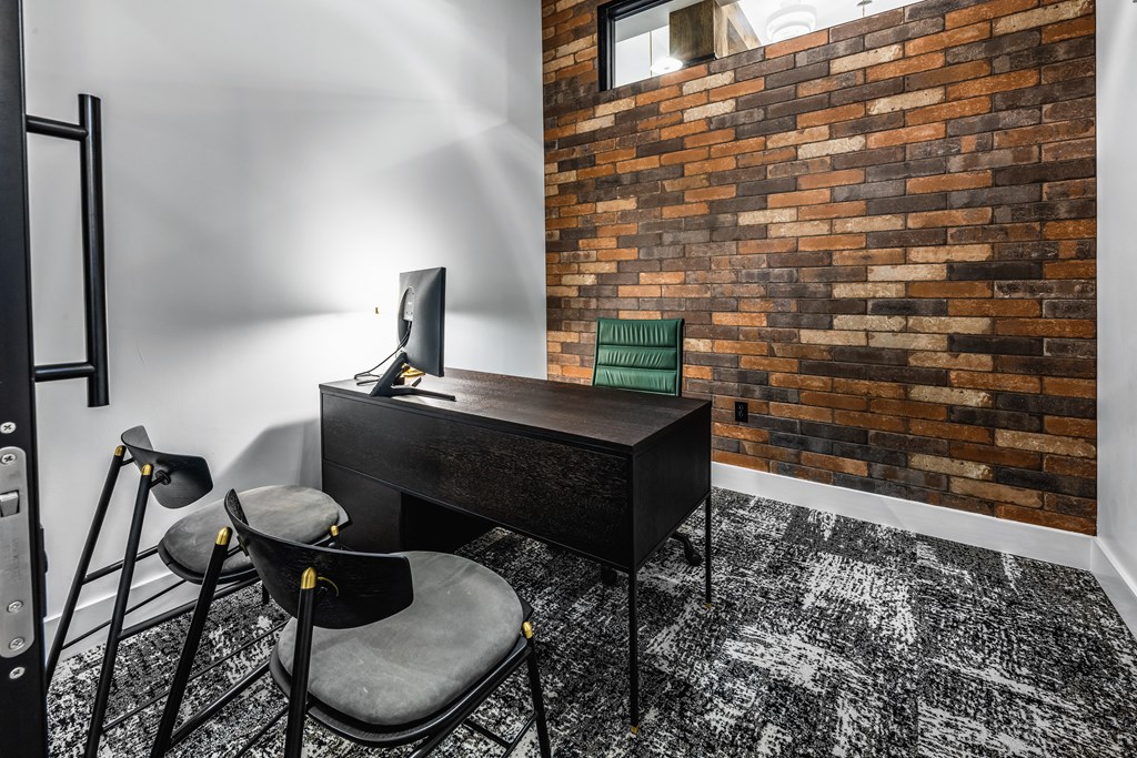 a home office with a desk and chairs and a brick wall