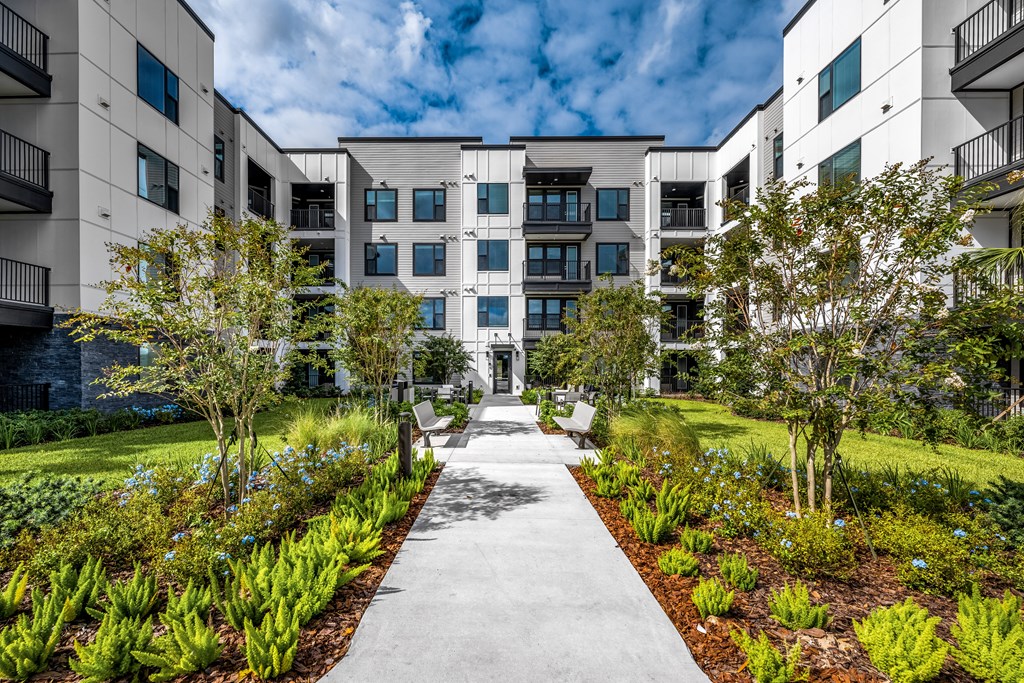 an exterior view of an apartment building with a sidewalk and landscaping at The Alibi at Lake Lilly, Ocoee, FL
