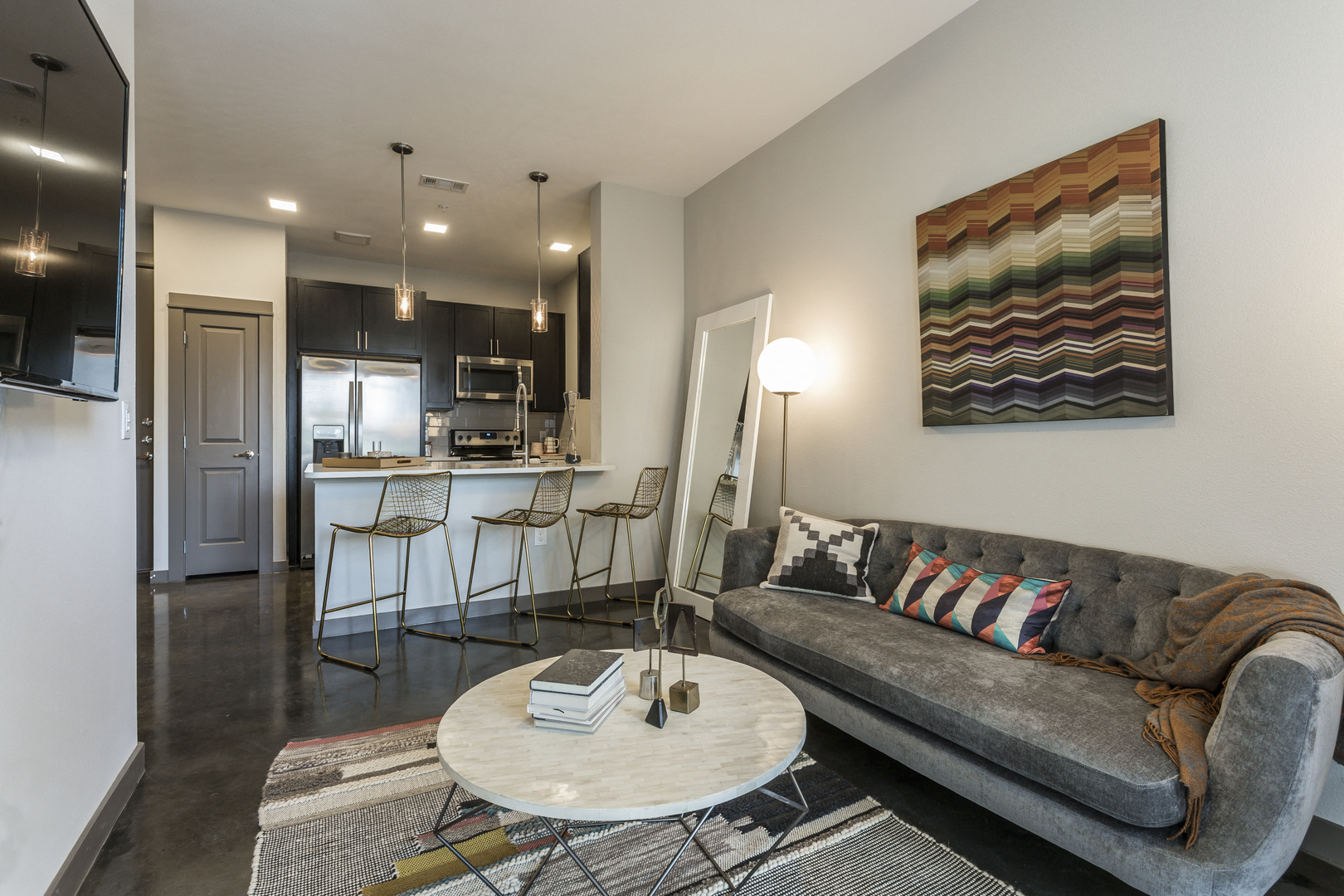A grey couch with a blanket on it sits in a living room with a white coffee table in front of it.