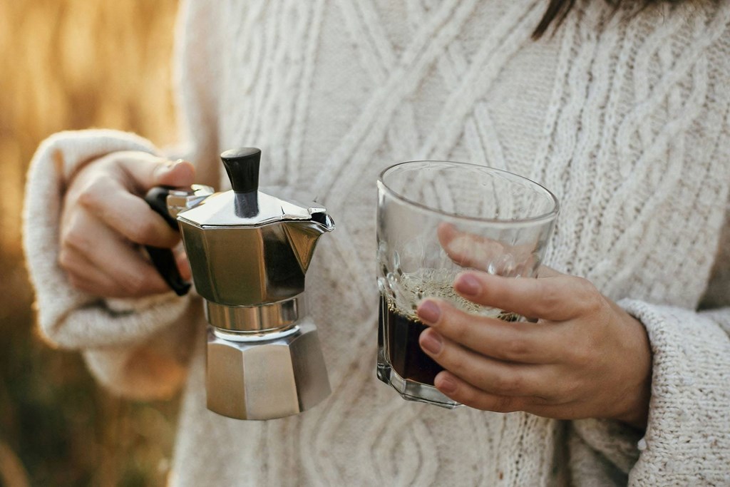 a woman holding a cup of coffee and a coffee maker