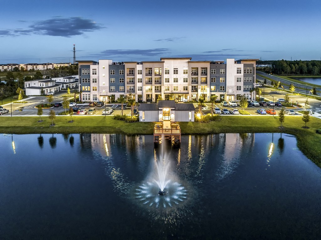 a fountain in the middle of a pond with an apartment building in the background at The Overlook, Winter Garden, 34787