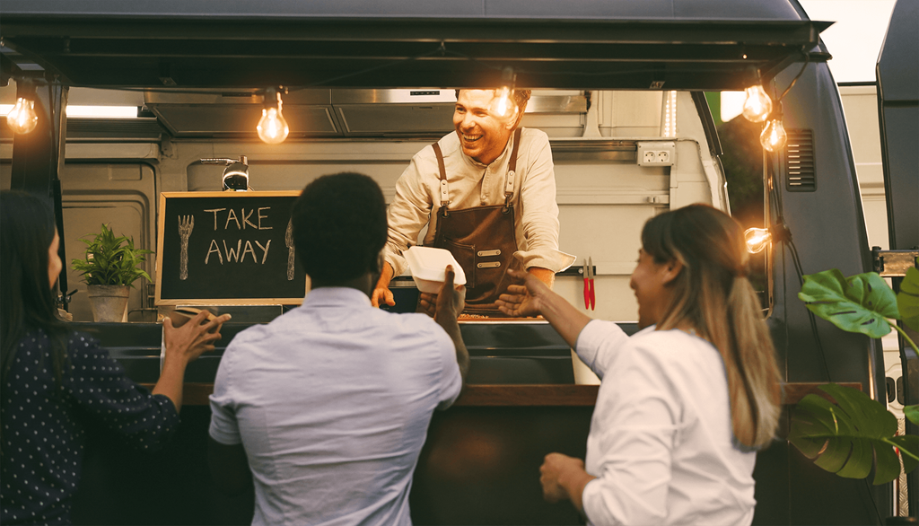 a man standing in a food truck selling food to three people