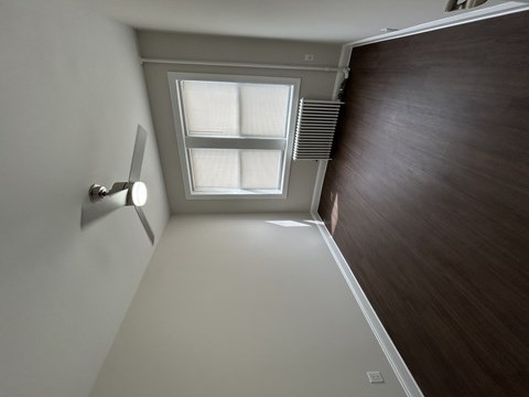 A room with a window and a light on the wall.