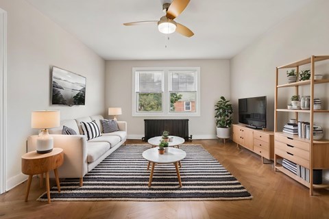 A living room with a white couch, a coffee table, a ceiling fan, and a bookshelf.