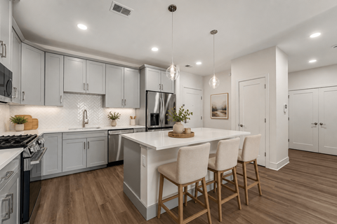 A modern kitchen with a white island and wooden chairs.