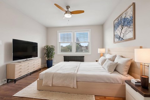 A bedroom with a large bed, a flat screen TV, and a ceiling fan.
