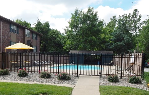 A pool surrounded by a black fence with a yellow umbrella and a building in the background.