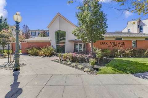 A building with a sign that says Oak Village is in front of some trees at Oak Village Apartments, Oakland, CA