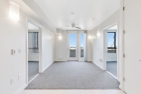 A spacious, empty room with a ceiling fan and carpeted floor.