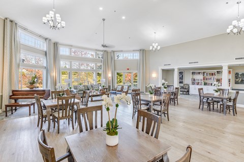 A room with wooden chairs and tables with a vase of flowers on the table in the center at Manor at Victoria Park, Temple Hills, 20748