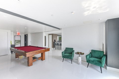 A room with a pool table, two green chairs and a small table.