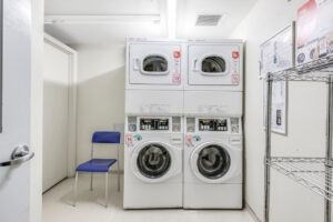 A laundry room with a stack of washing machines and a blue chair.