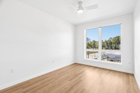 A room with a ceiling fan and a large window overlooking a parking lot.