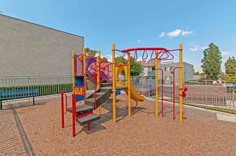 A playground with a red and yellow swing set.