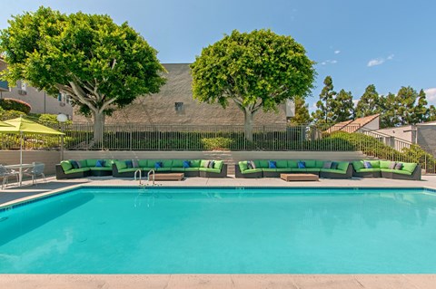 A large swimming pool with a green bench and trees in the background.